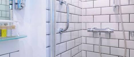 A modern bathroom with white subway tiles, a glass shower enclosure, a white sink, and a glass shelf with toiletries.