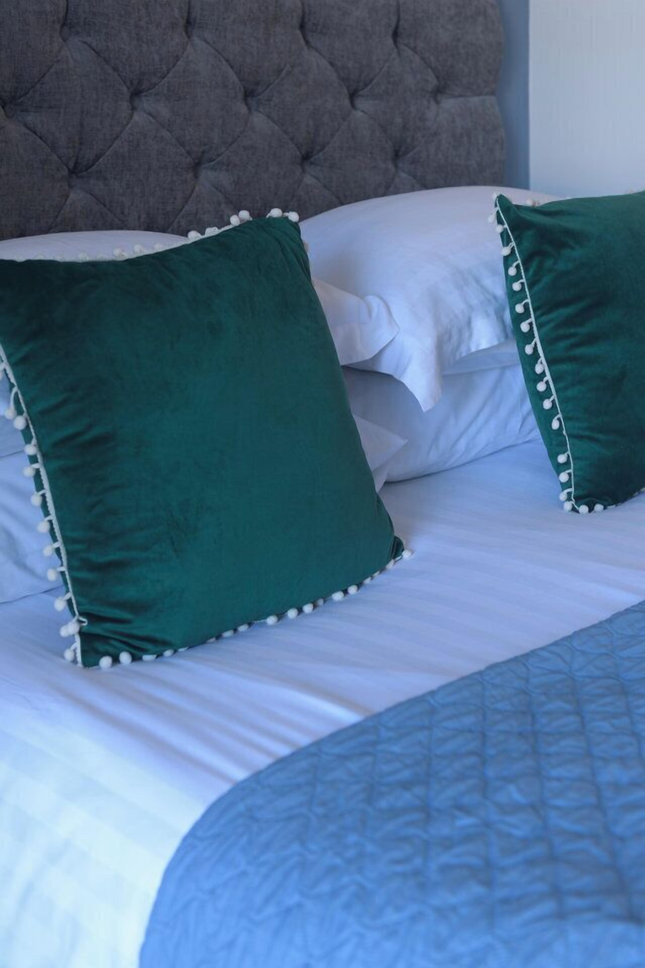 A bed with white linens and green pillows with white trim.