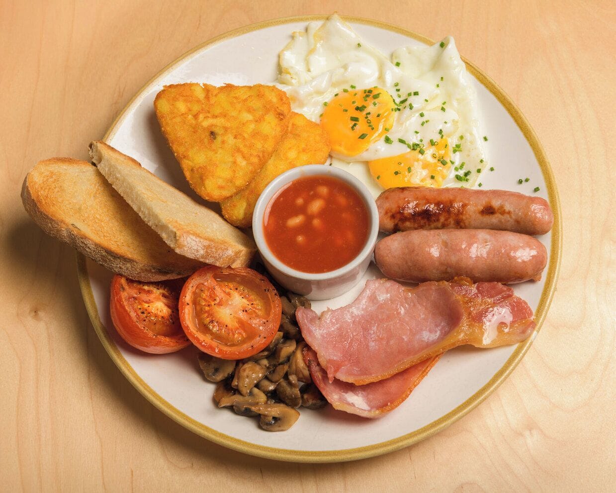 A plate of breakfast food including eggs, sausages, bacon, tomatoes, mushrooms, toast, and beans.
