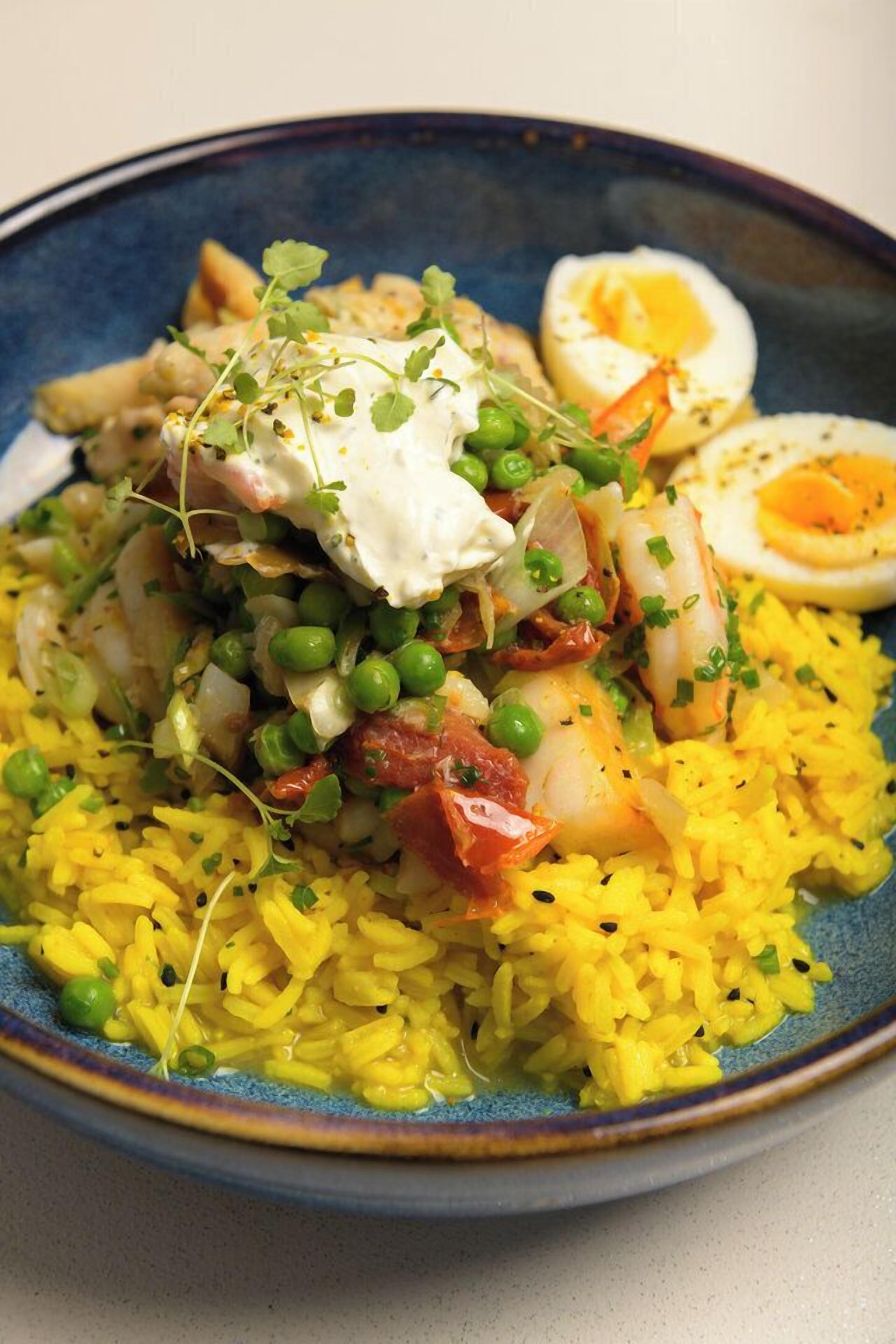 A plate of yellow rice with green peas, bacon, and a poached egg on top.