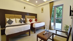 A hotel room with two beds, a small table, a chair, a TV, and a window with a view of trees. - A K G Hotel (Puducherry)
