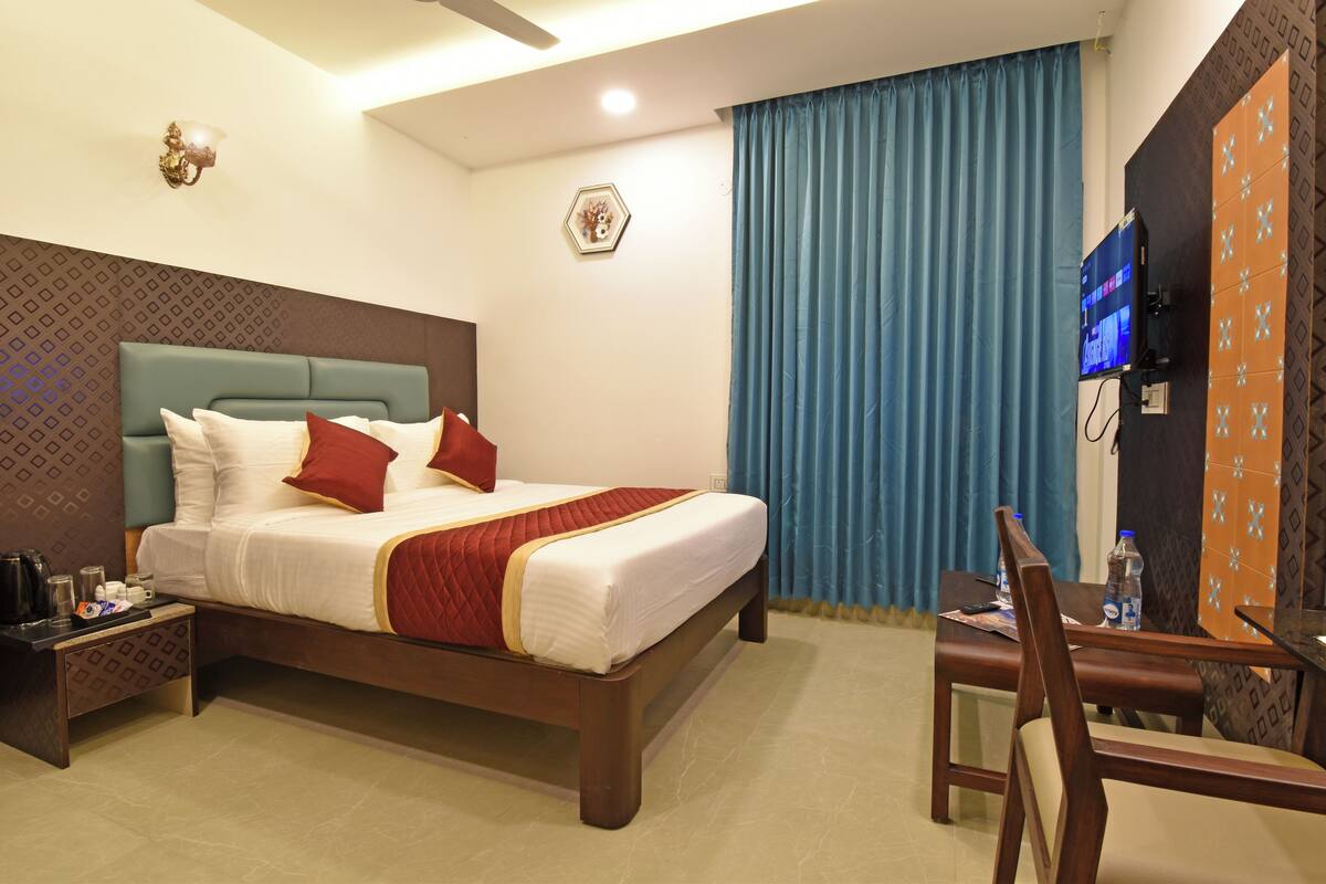 Ein Hotelzimmer mit Bett, Nachttisch, Stuhl, Fernseher und Vorhängen.