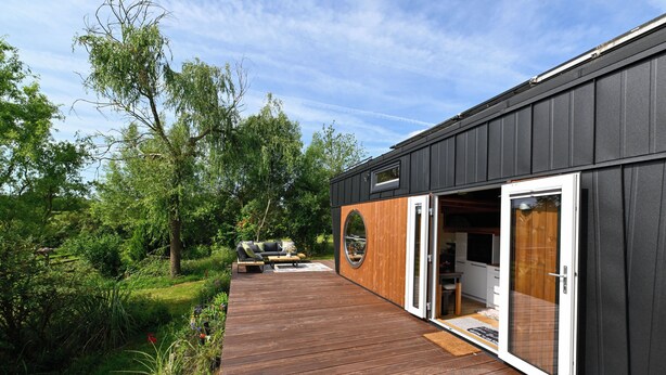Un bâtiment moderne doté d’une terrasse en bois, d’une fenêtre circulaire et d’une porte donnant accès à un espace intérieur.