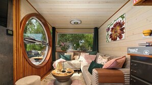 Une pièce chaleureuse avec une fenêtre ronde, un plafond en bois, un ensemble de canapés, une table basse et une commode.