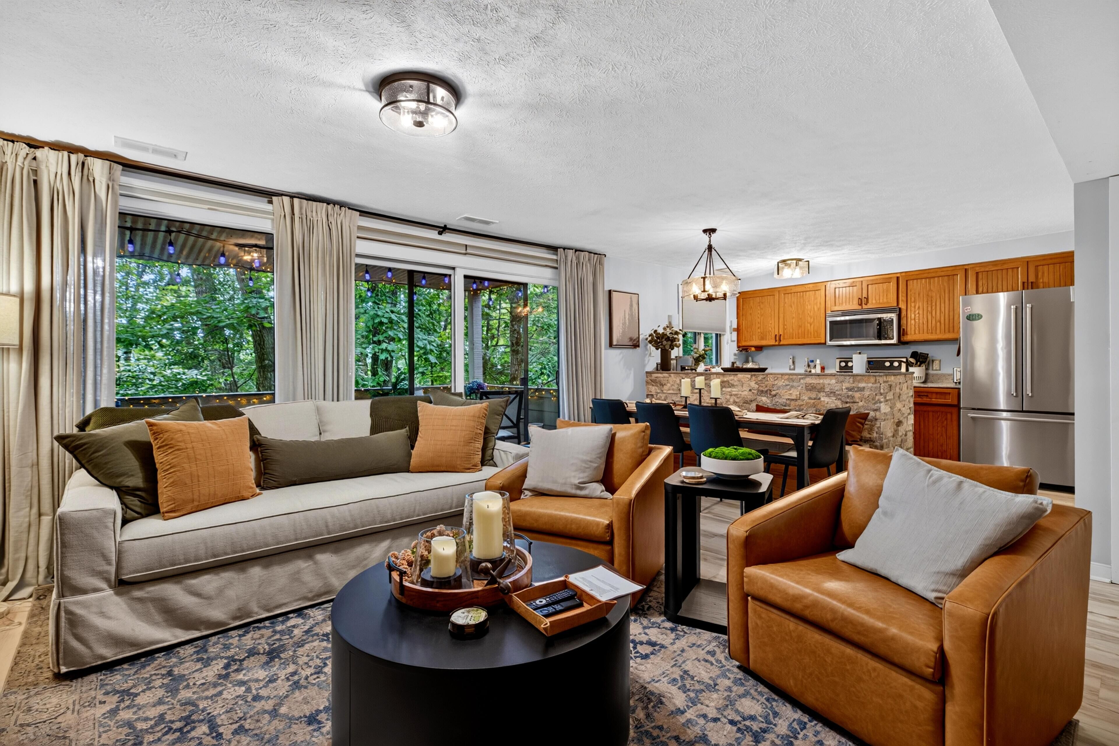 A modern living room with a sofa, chairs, a coffee table, and a kitchen area with wooden cabinets and appliances.