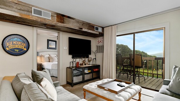 A living room with a sofa, a coffee table, a TV, and a wooden ceiling. There is a sign that says "Eat Sleep Ski" and a sign that says "Blue Mountain Barrel House".