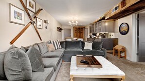 A modern living room with a sectional sofa, a coffee table, and a kitchen in the background.