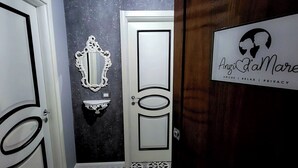 A hallway with a door, a wall-mounted mirror, and a sign with a silhouette and text. - Love nest with Jacuzzi and Terrace on the Port of Anzio (Anzio)