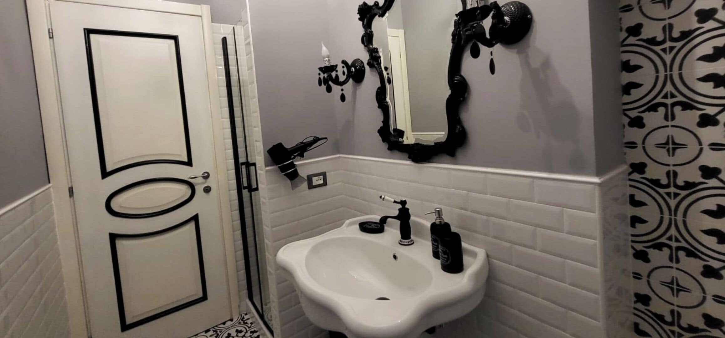 A bathroom with a white sink, a mirror with black dripping paint, and a patterned wall.