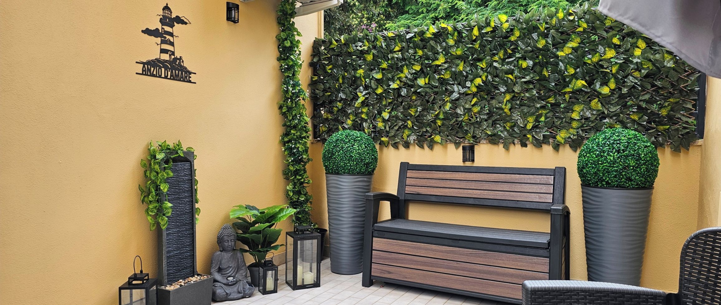 Un banc agrémenté d’un coussin, entouré de plantes en pot et adossé à un mur recouvert d’une plante grimpante.