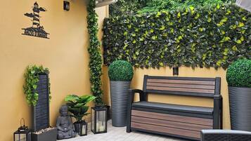 Un banc agrémenté d’un coussin, entouré de plantes en pot et adossé à un mur recouvert d’une plante grimpante.