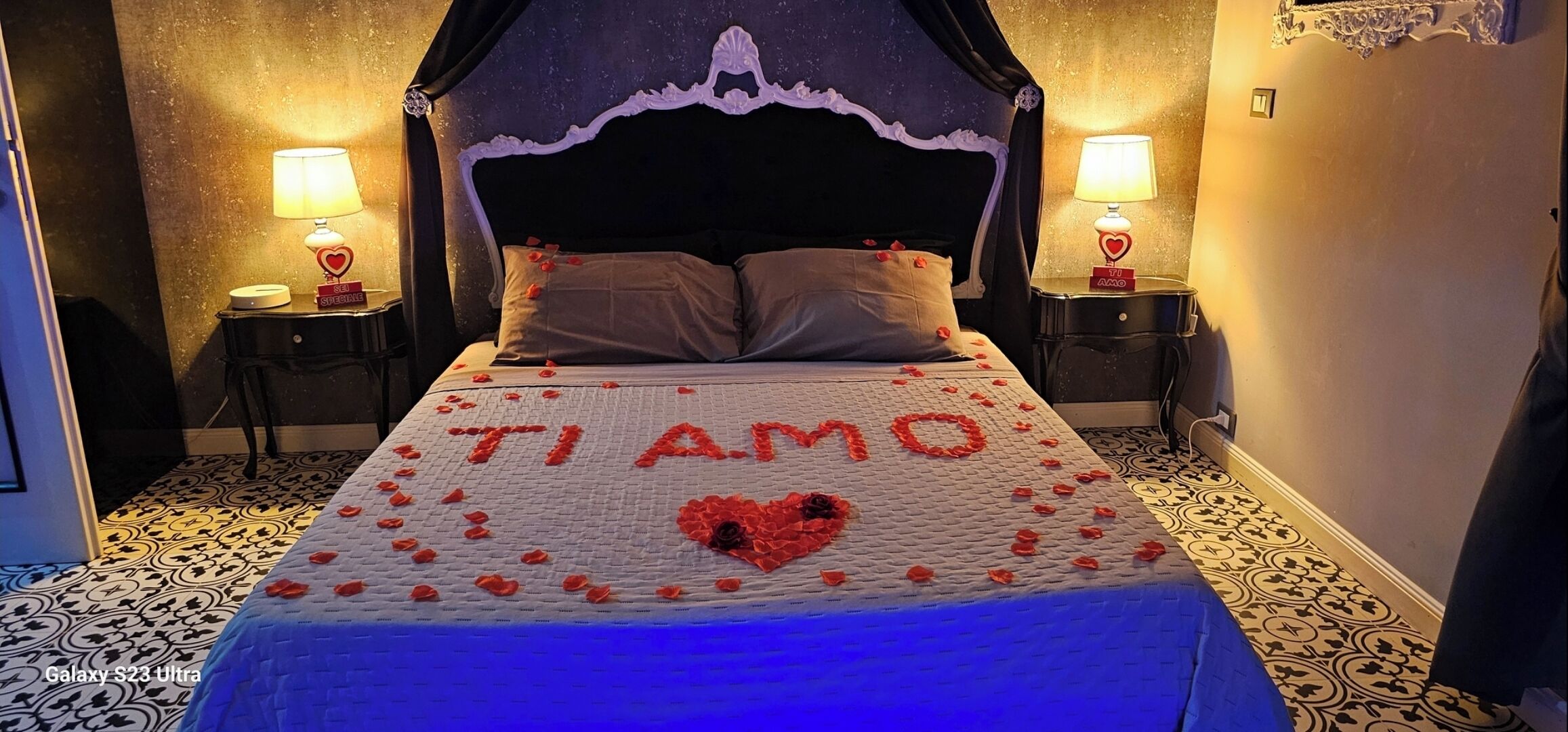 Ein Bett mit Baldachin, eine herzförmige Dekoration auf der Bettdecke und ein Schild mit der Aufschrift 'TIAMO'.