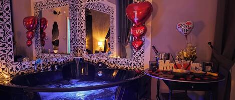 Un baño lujoso con una bañera grande, un espejo con marco decorativo y globos con forma de corazón.