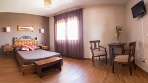 A bedroom with a wooden bed, bedside tables, a small round table with chairs, a TV mounted on the wall, and a window with curtains. - Callejón del Pozo I. (Gálvez)