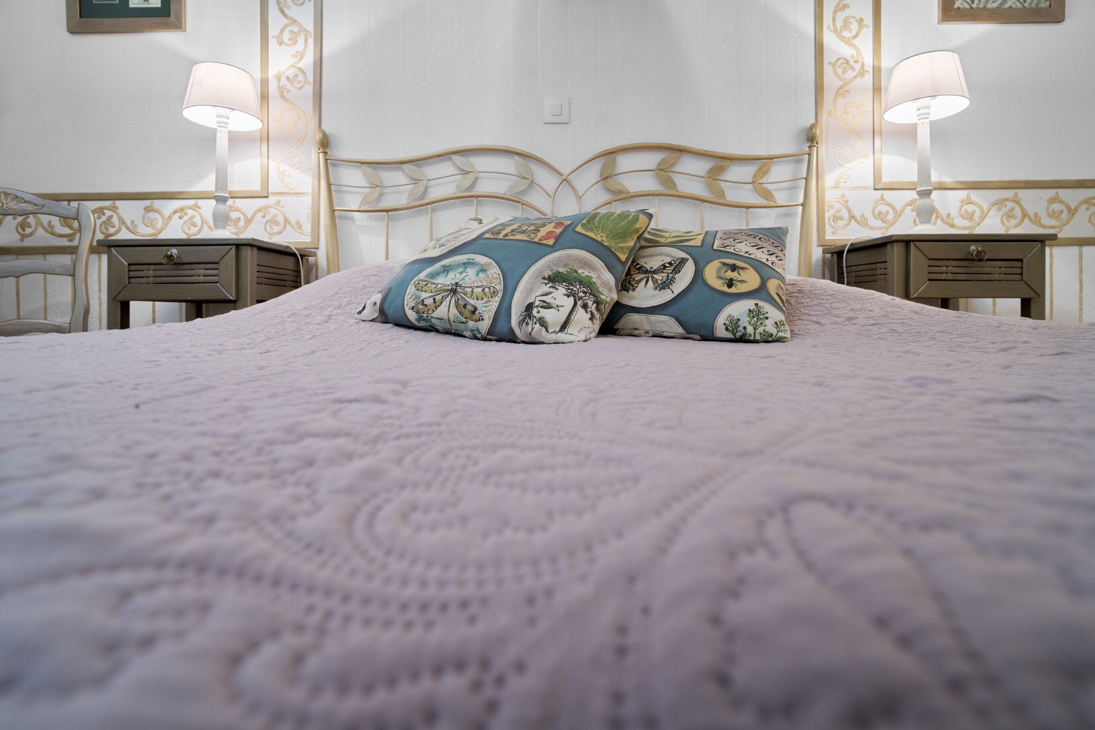 A bed with a patterned bedspread, two decorative pillows, a headboard, bedside tables with lamps, and a wall with a decorative panel.
