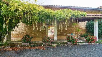 Un edificio con fachada de piedra, techo de tejas y plantas colgantes. Hay macetas con flores rojas en el frente del edificio.