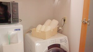Un lavadero pequeño equipado con lavadora, microondas y una cesta de toallas.