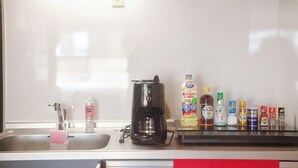 Una cocina con un lavamanos, una cafetera y varios condimentos sobre la encimera.