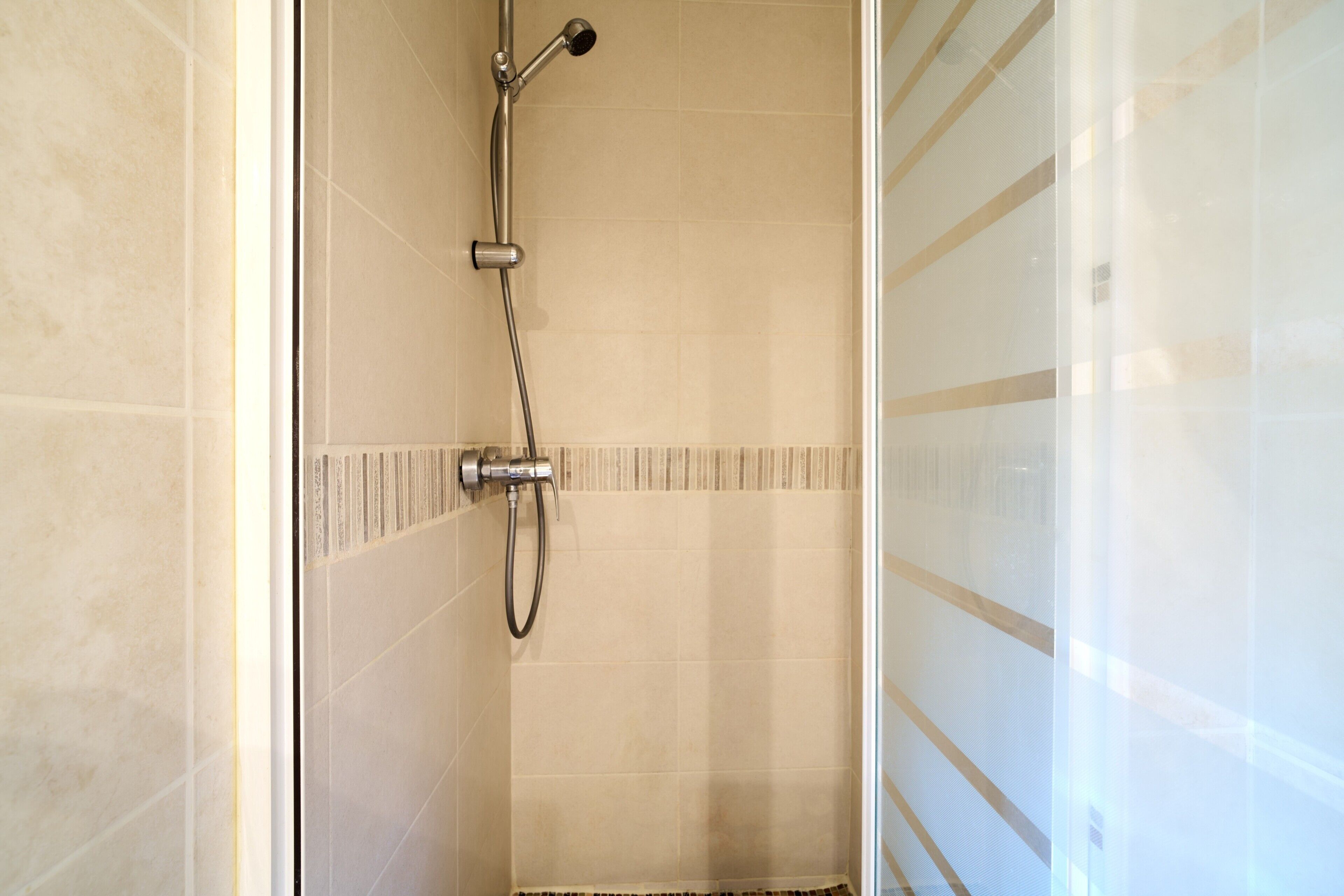 Une douche fermée par des parois en verre, dotée d’un pommeau de douche à main et d’un robinet mural.