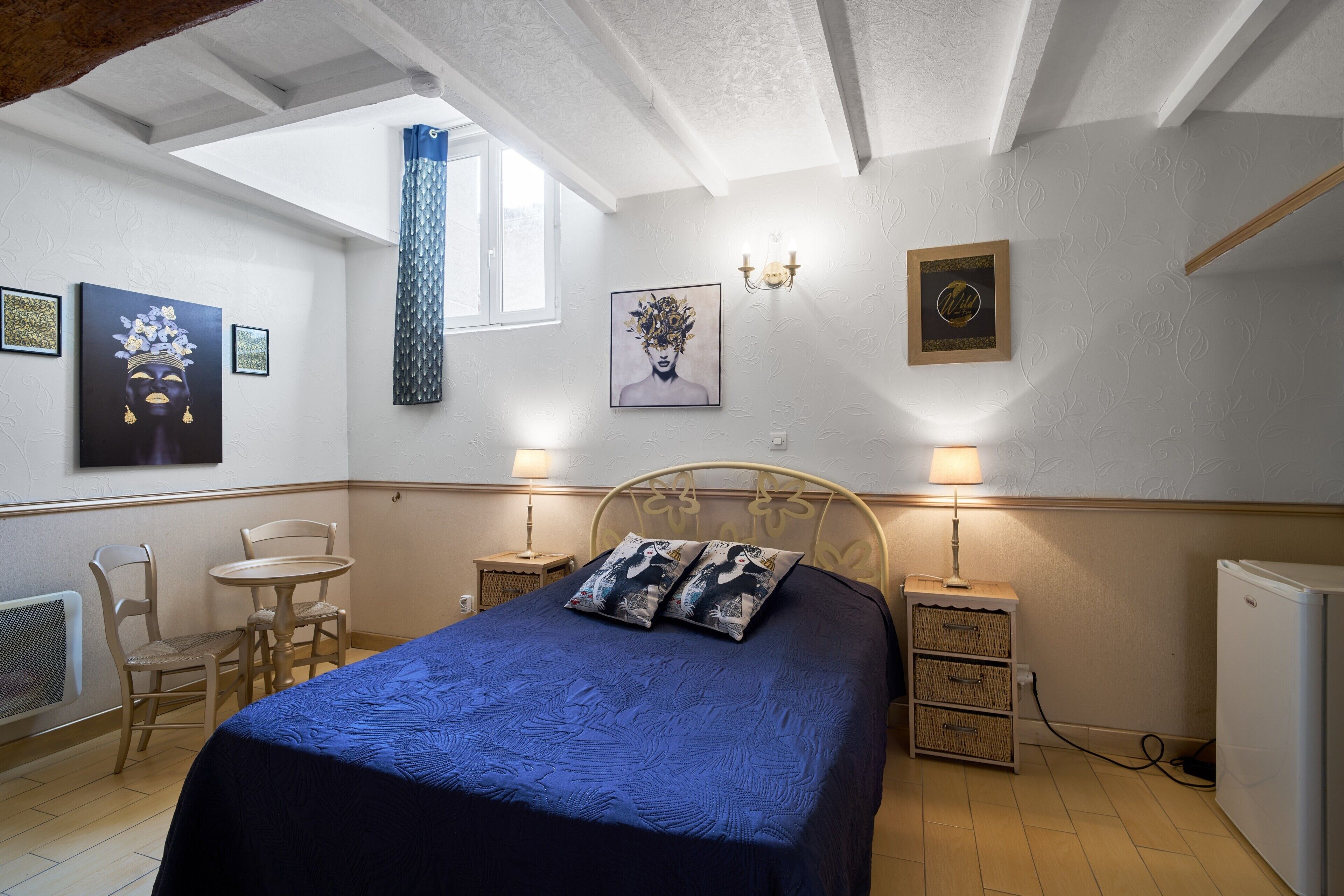 Ein Schlafzimmer mit einem Bett, zwei Nachttischen, einem Sessel, einer Lampe und Kunstwerken an den Wänden.