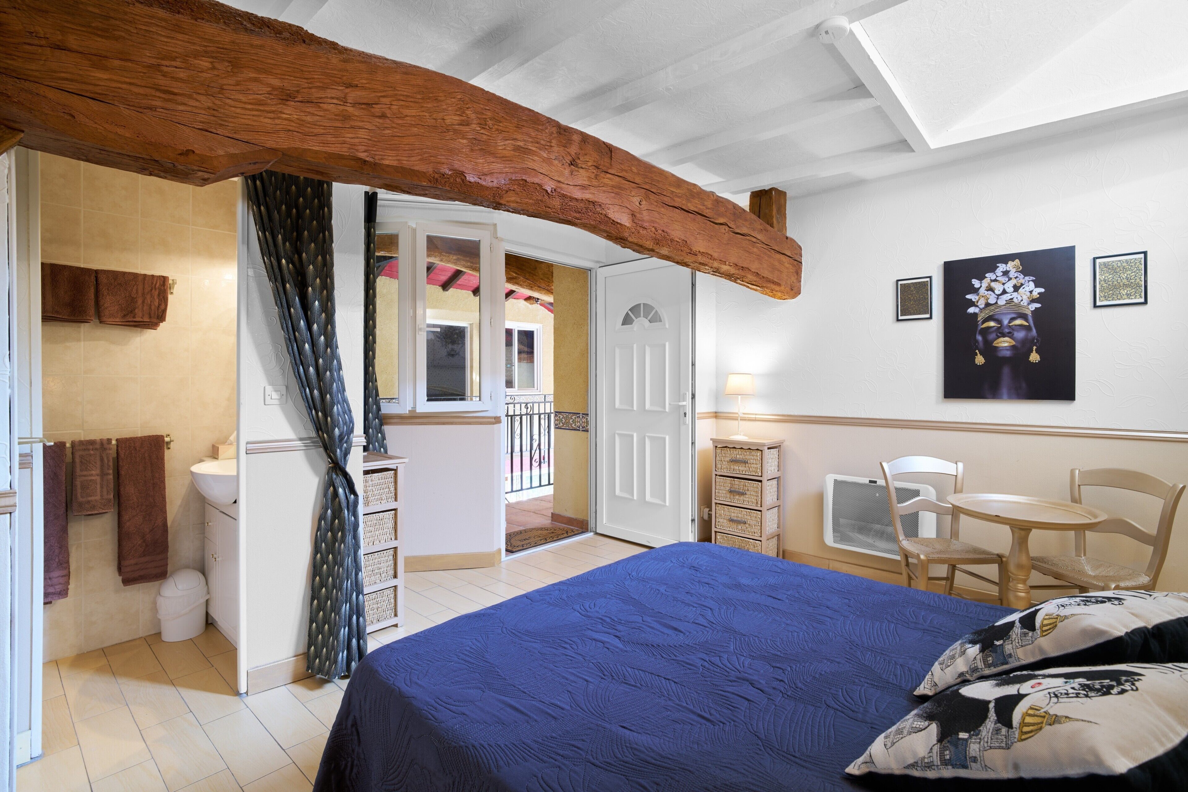 A bedroom with a bed, a wooden ceiling beam, a bathroom, and a balcony.