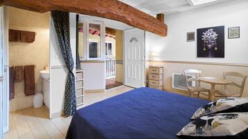 Une chambre avec un lit, une poutre en bois au plafond, une salle de bain et un balcon.