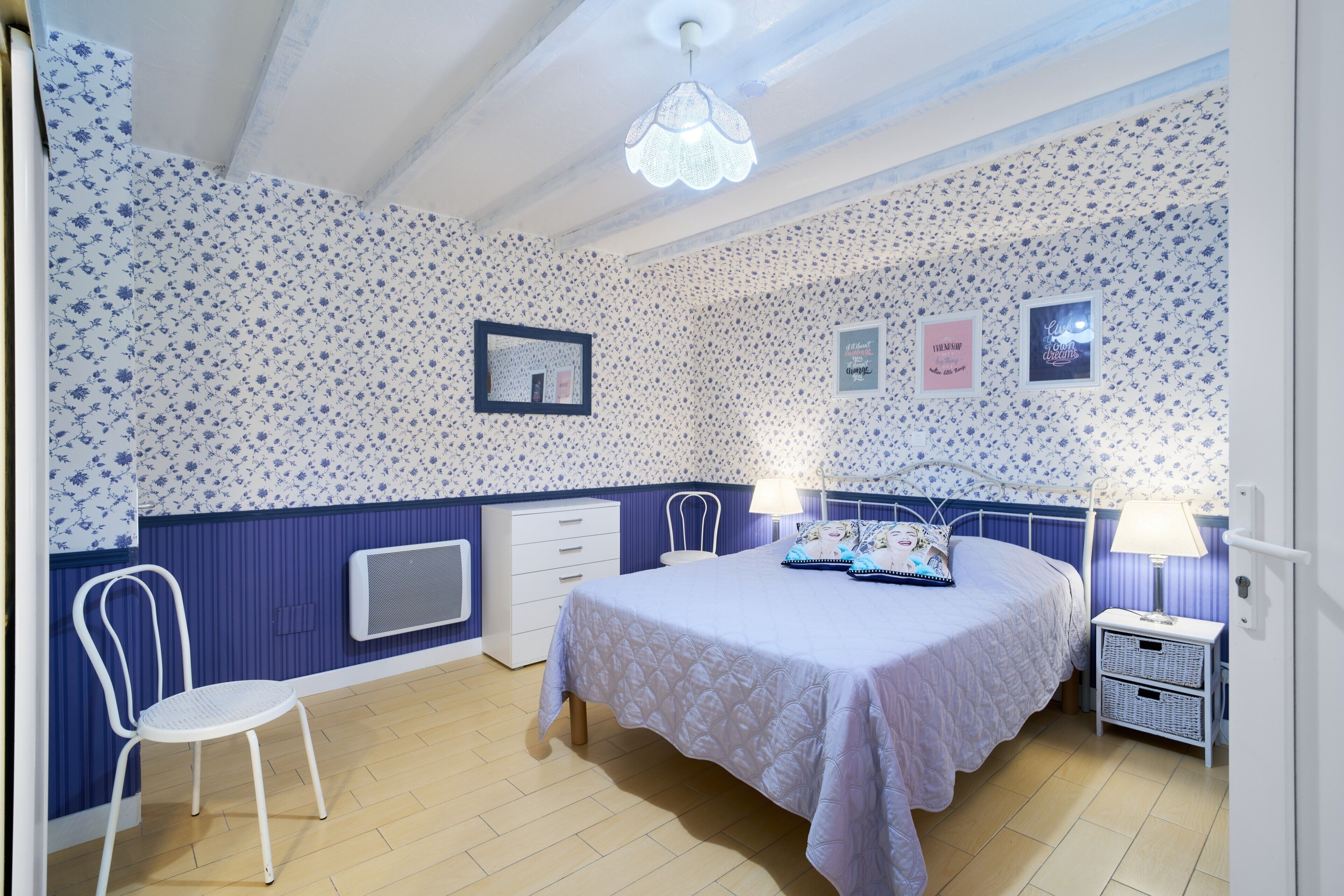 A bedroom with a bed, a chair, a nightstand, and a wall with floral wallpaper.