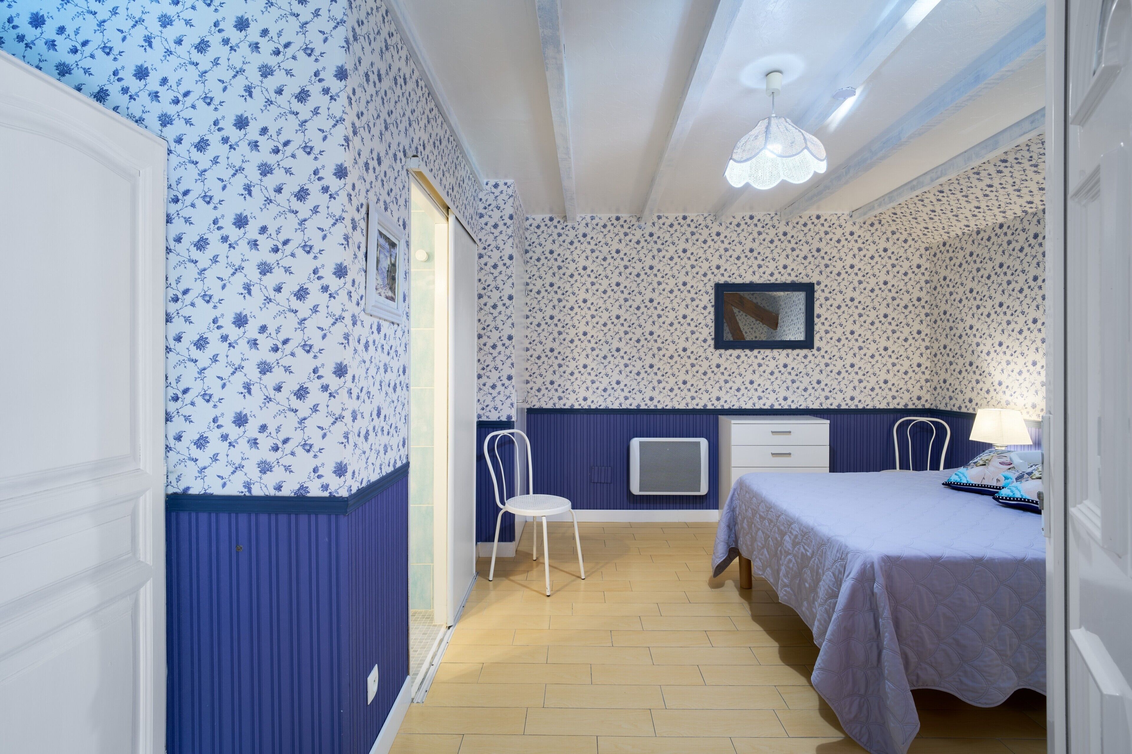 Une pièce avec un papier peint à motifs floraux, un lit, une chaise, une table de chevet et une fenêtre.