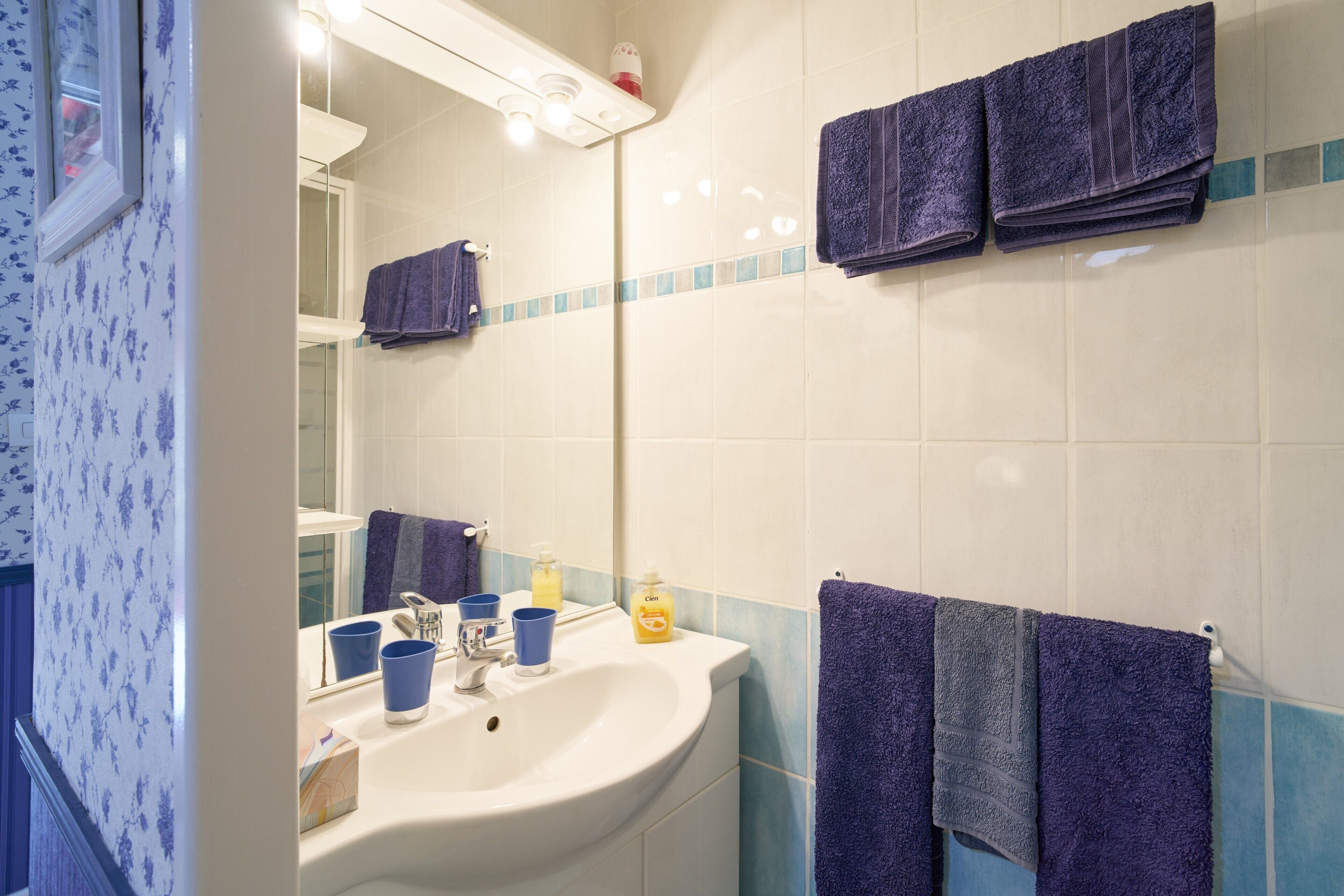 A bathroom with a sink, mirror, and multiple towels.