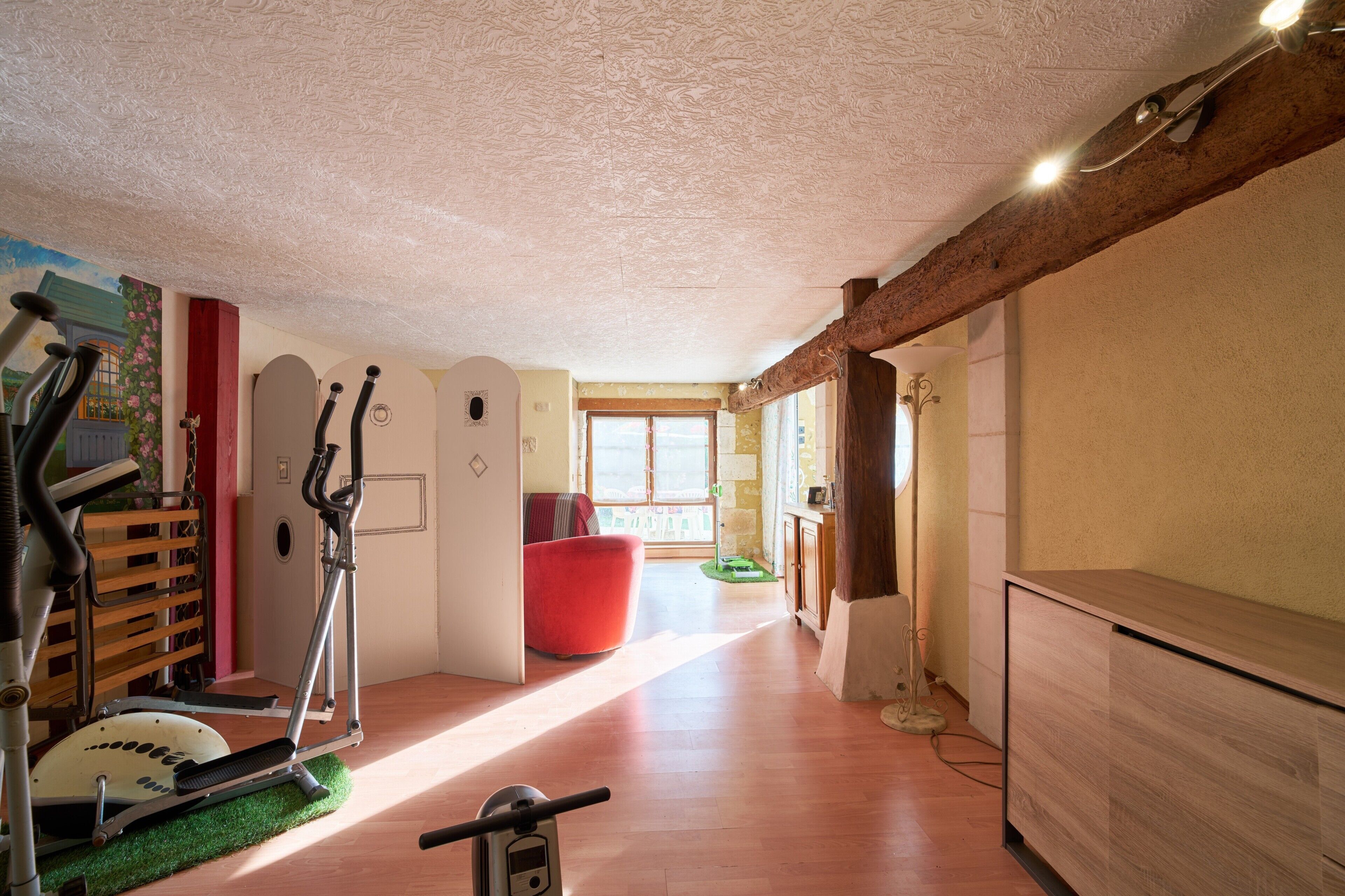 A room with a treadmill, a red chair, a wooden cabinet, and a window with natural light.