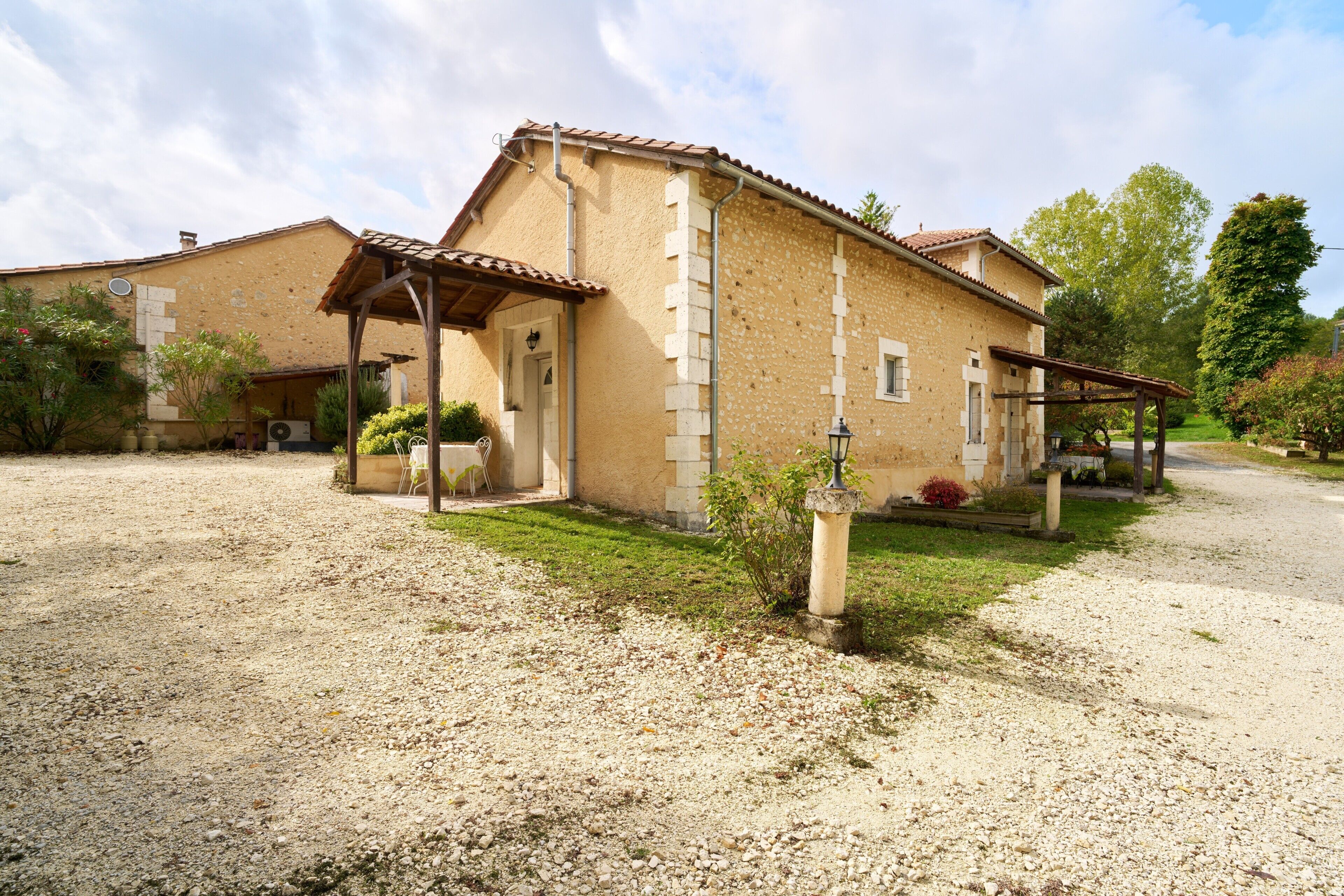 Un bâtiment à deux étages avec une allée en gravier, un porche couvert et un petit jardin.