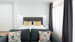 A hotel room with a large bed, two bedside tables, a sofa with floral cushions, and a window with curtains.