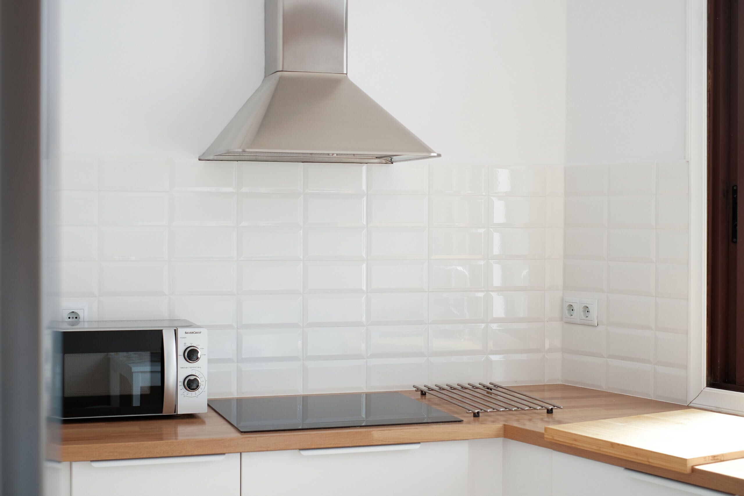 Una cocina con microondas, extractor de acero inoxidable y encimera de madera.