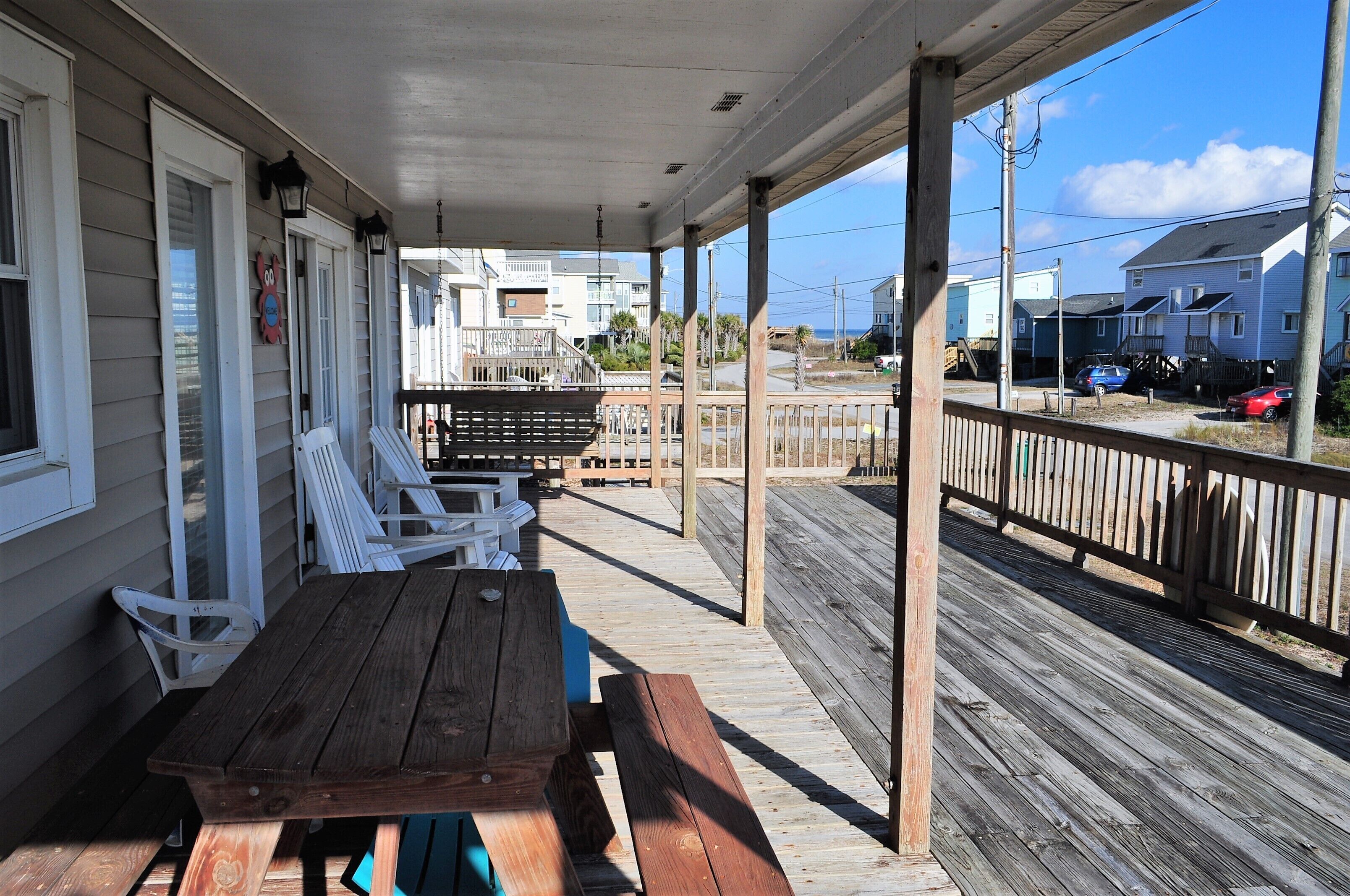 A covered outdoor area with a wooden deck, white chairs, and a picnic table.