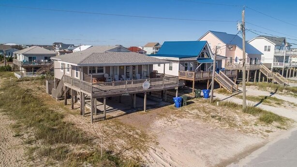 Et hus ved stranden med en terrasse, en overdækket veranda og en trappe til hovedbygningen.