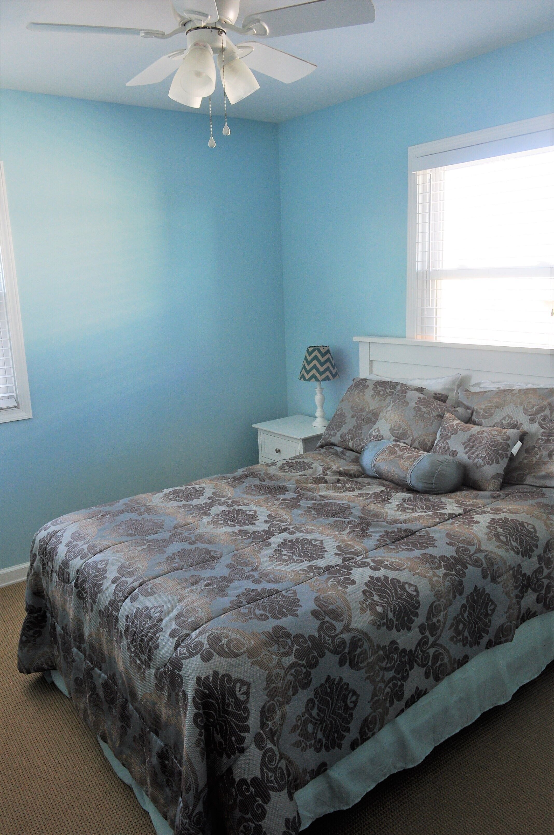 A bedroom with a bed, a nightstand, a lamp, a ceiling fan, and a window.