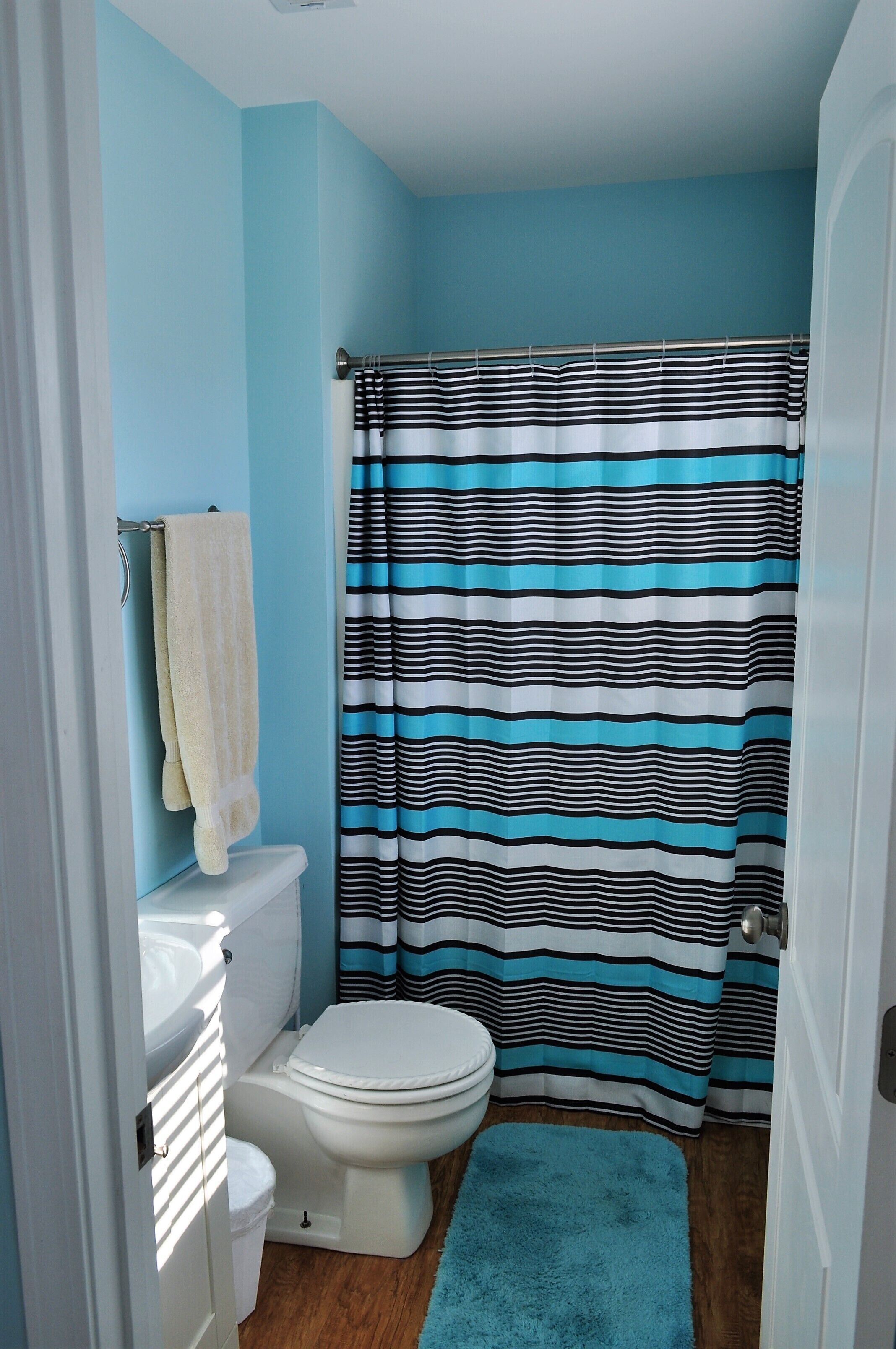 A bathroom with a striped shower curtain, a white toilet, and a blue rug.