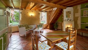 A rustic kitchen with wooden beams, a dining area with a table and chairs, and a staircase leading to a loft. - Charming Gîte "L'Atelier": Your Périgord Retreat with Shared Pool, Private Terrace & Wi-Fi (Saint-Sulpice-de-Roumagnac)