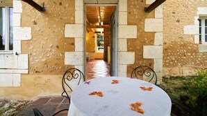 A table with a white tablecloth and orange flowers, set against a building with a stone facade and a doorway leading to an interior space. - Charming Gîte "L'Atelier": Your Périgord Retreat with Shared Pool, Private Terrace & Wi-Fi (Saint-Sulpice-de-Roumagnac)