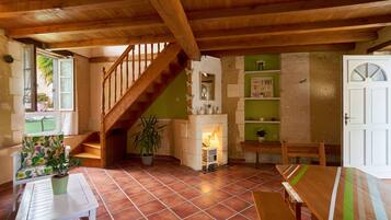 A rustic interior with a wooden staircase, a dining table, a bench, and a potted plant.