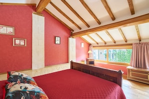 Ein Schlafzimmer mit Holzbalkendecke, einer roten Bettdecke und einem Fenster mit Vorhängen.