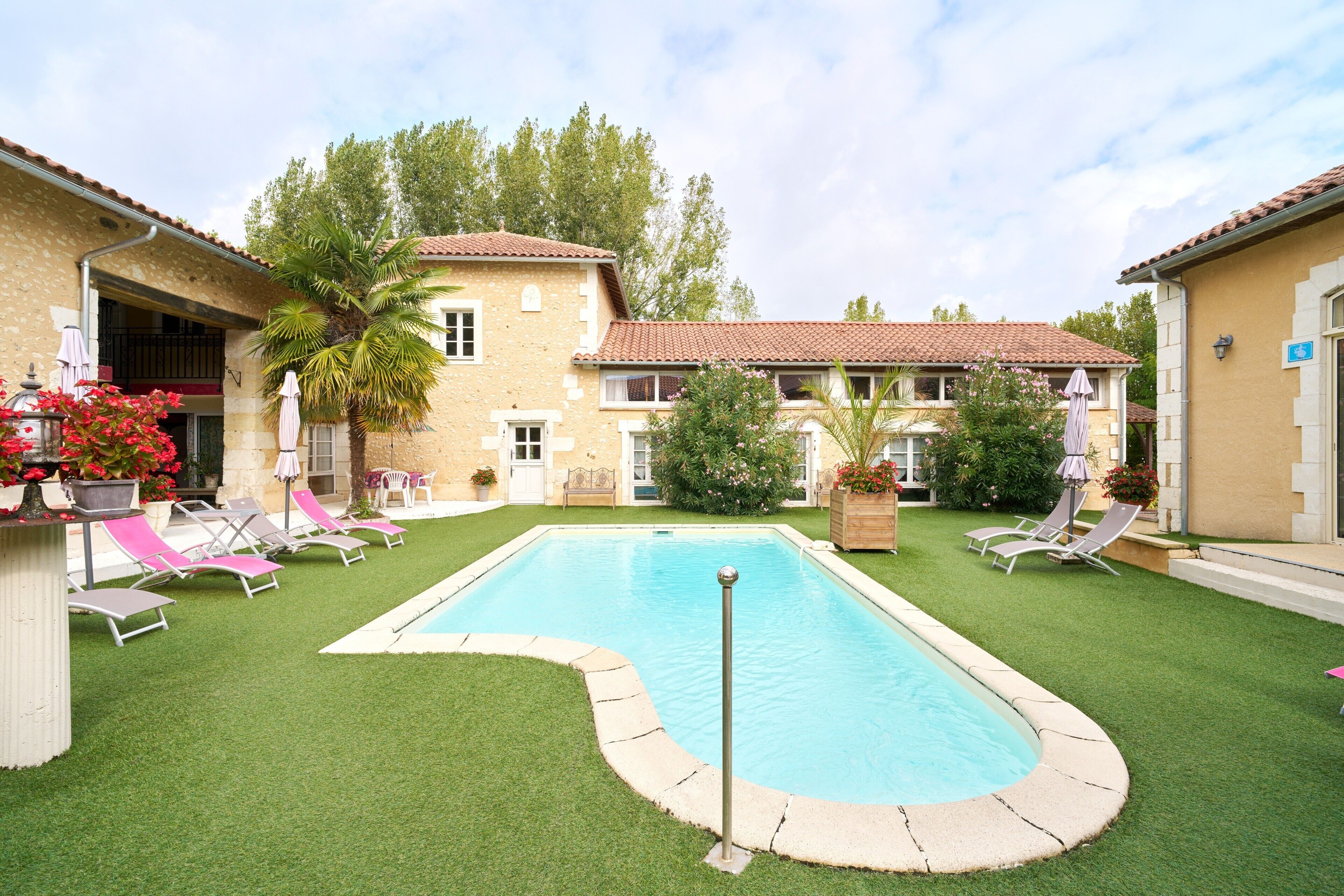 A swimming pool surrounded by artificial grass, with lounge chairs and a palm tree.