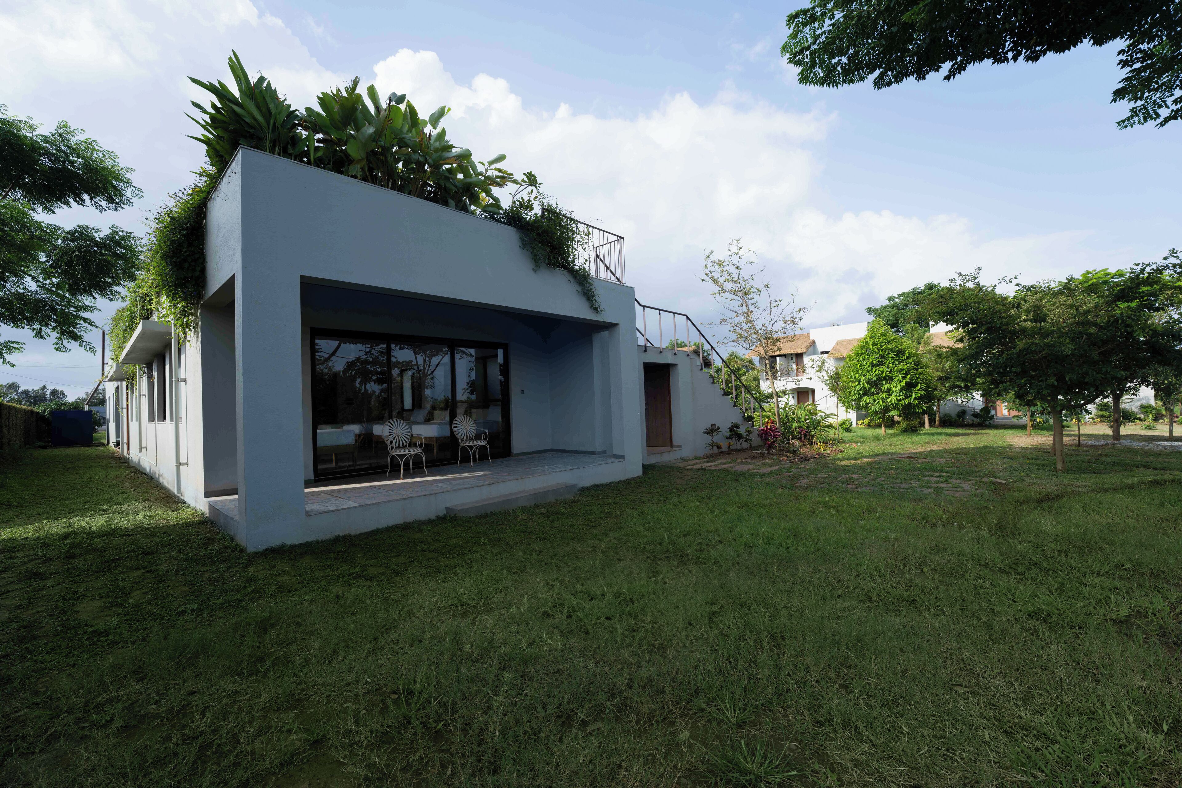 A modern house with a flat roof, large windows, and a small outdoor seating area.
