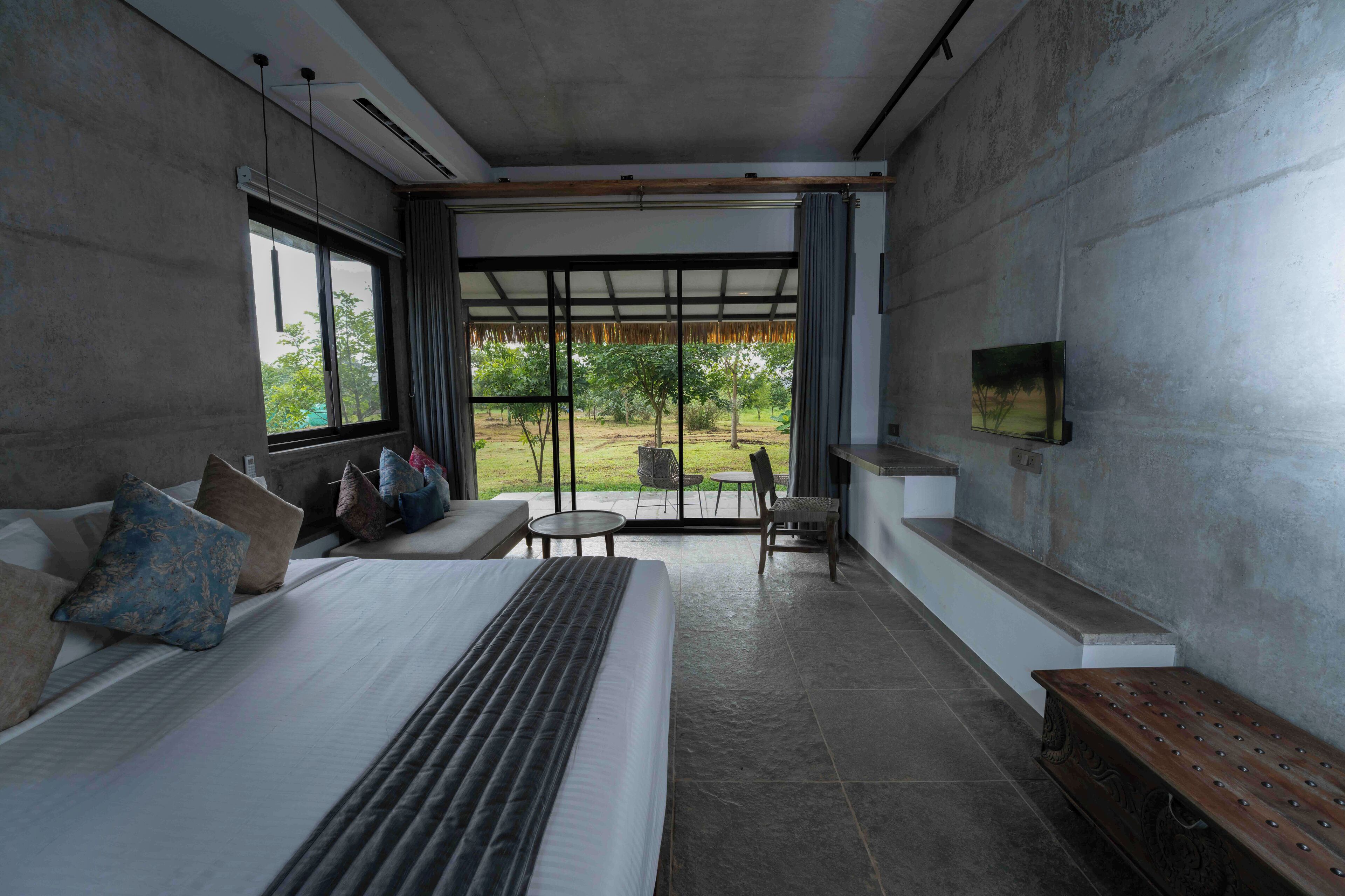 Une chambre moderne avec un grand lit, un téléviseur fixé au mur et une vue sur l’extérieur grâce à une grande fenêtre.