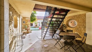 A patio area with a concrete floor, a wooden table, metal chairs, a spiral staircase, and a stone wall. - Charming Gîte 'Le Pigeonnier' – Your Retreat in Périgord (Saint-Sulpice-de-Roumagnac)
