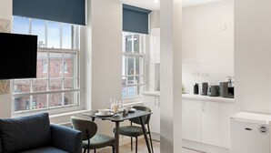 A modern kitchen with white cabinets, a dining area with a table set for two, and a sofa.