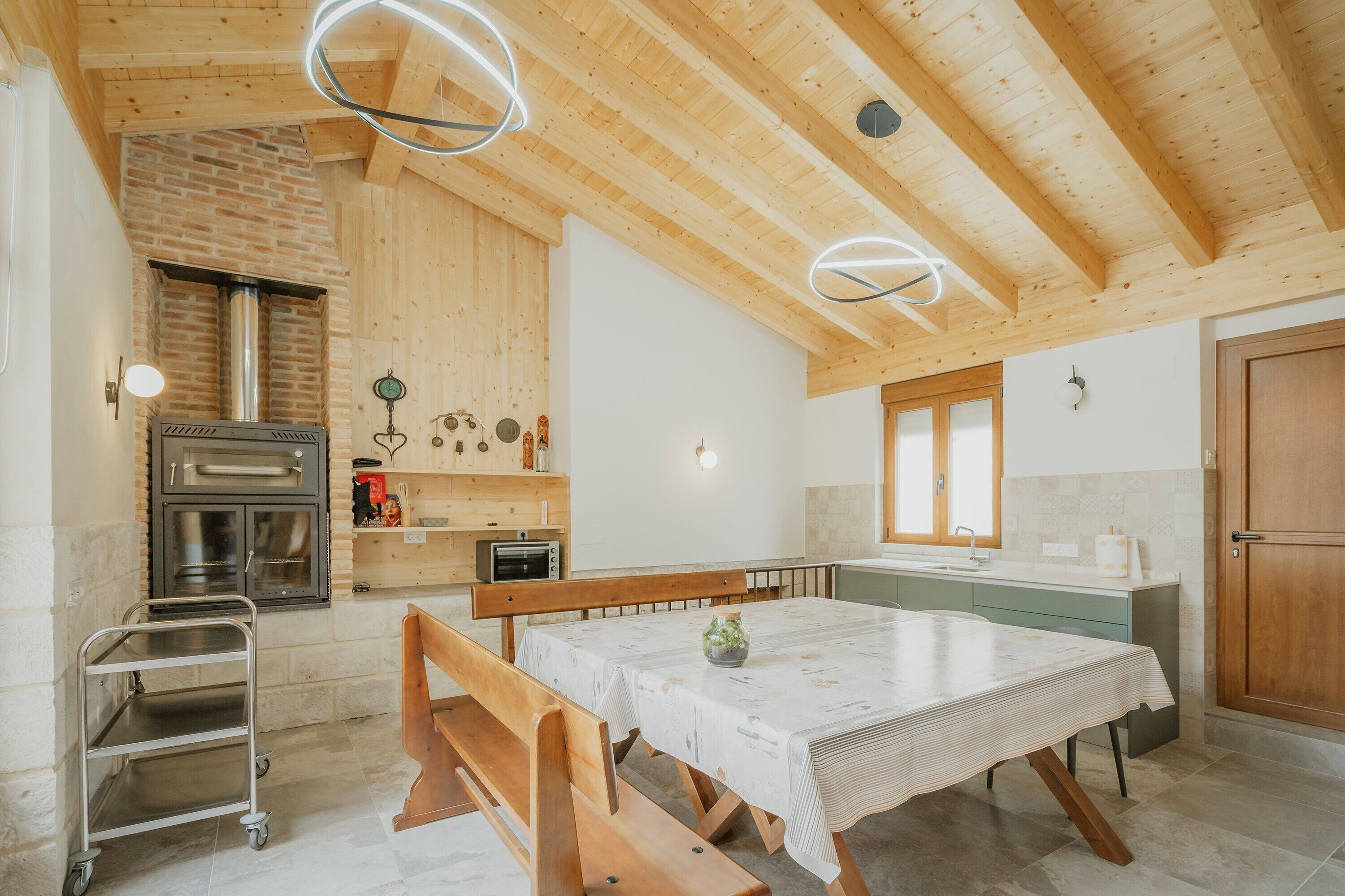 Una cocina con vigas de madera, pared de ladrillo, estufa y una mesa de comedor con bancos.
