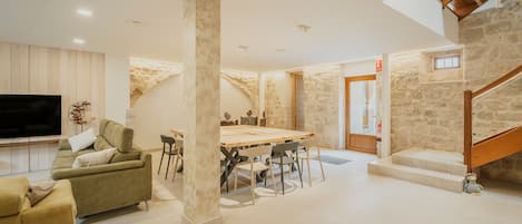 A spacious living area with a dining table, sofa, and a staircase leading to an upper level.