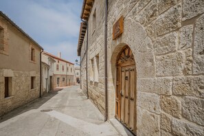 A narrow street with stone buildings, a wooden door, and a clear sky. - Casa Rural Vallehermoso (Los Balbases)