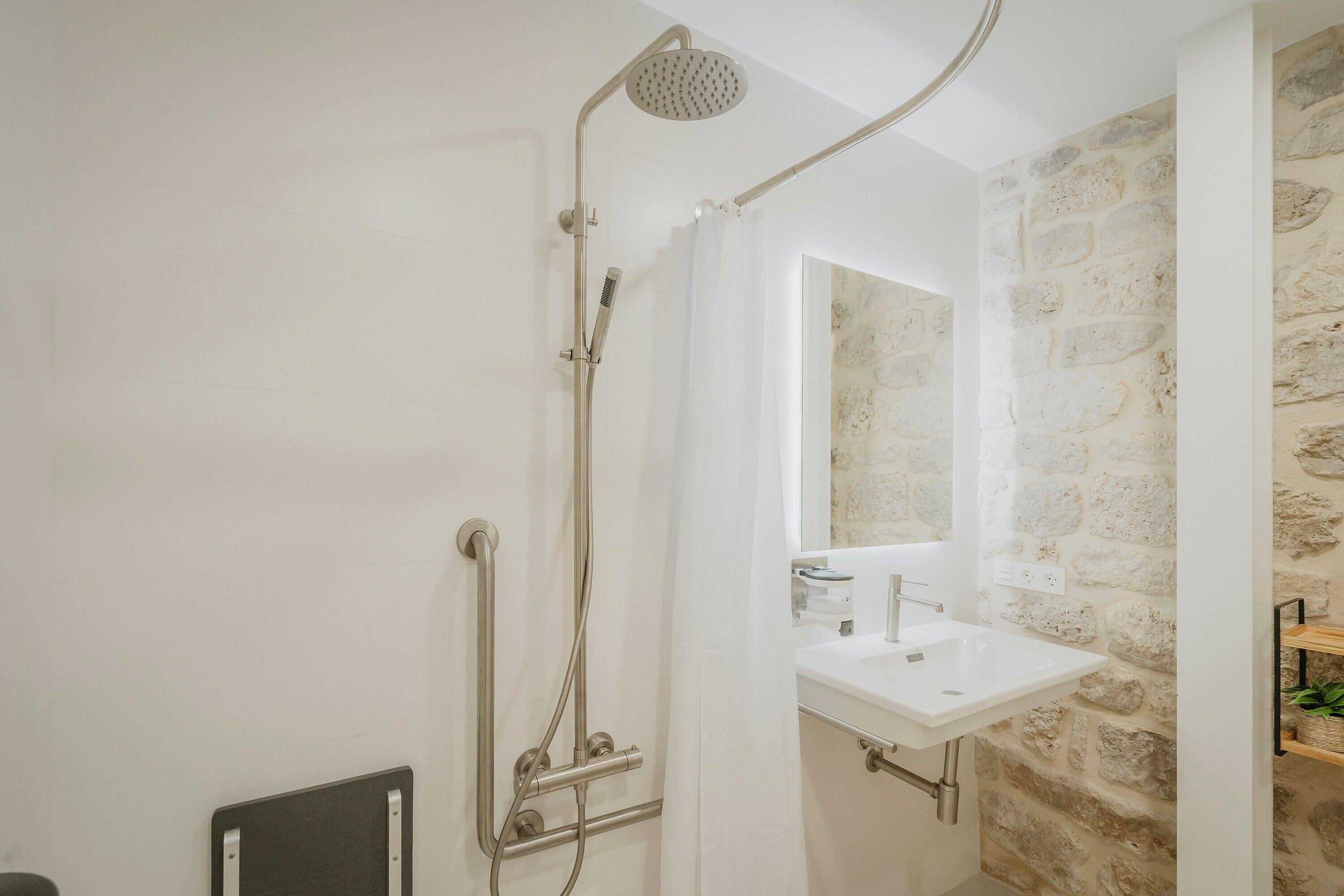 Una ducha con cabezal de ducha de mano, un lavabo blanco y una pared de piedra.